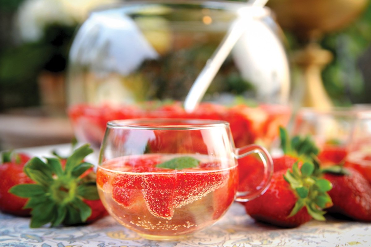 Ein Glas Erdbeerbowle vor einem Bowletopf.