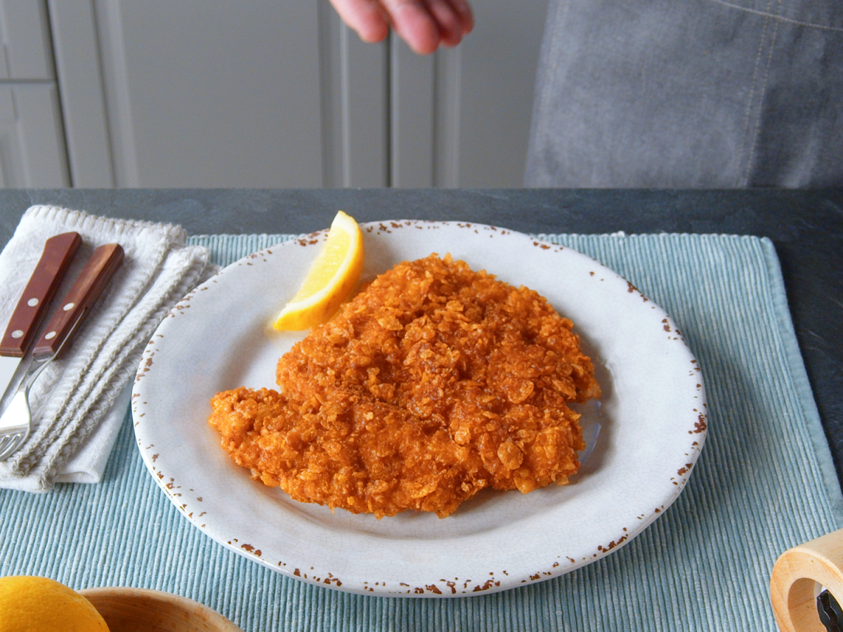 Hähnchenschnitzel mit Cornflakes-Panade auf einem Teller. Daneben liegt eine Zitrone.