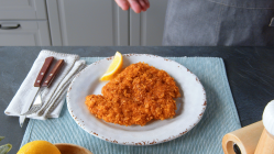 Hähnchenschnitzel mit Cornflakes-Panade auf einem Teller. Daneben liegt eine Zitrone.