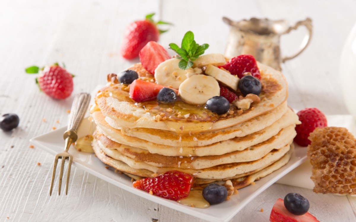 Ein Stapel Pancakes ohne Ei, mit Beeren, Nüssen und Ahornsirup.