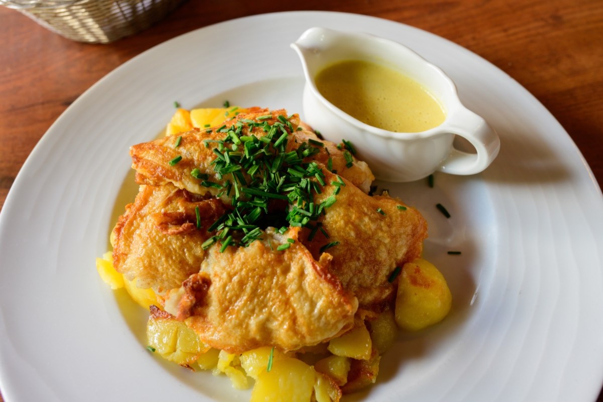 Pannfisch mit Bratkartoffeln und Senfsoße auf einem weißen Teller.