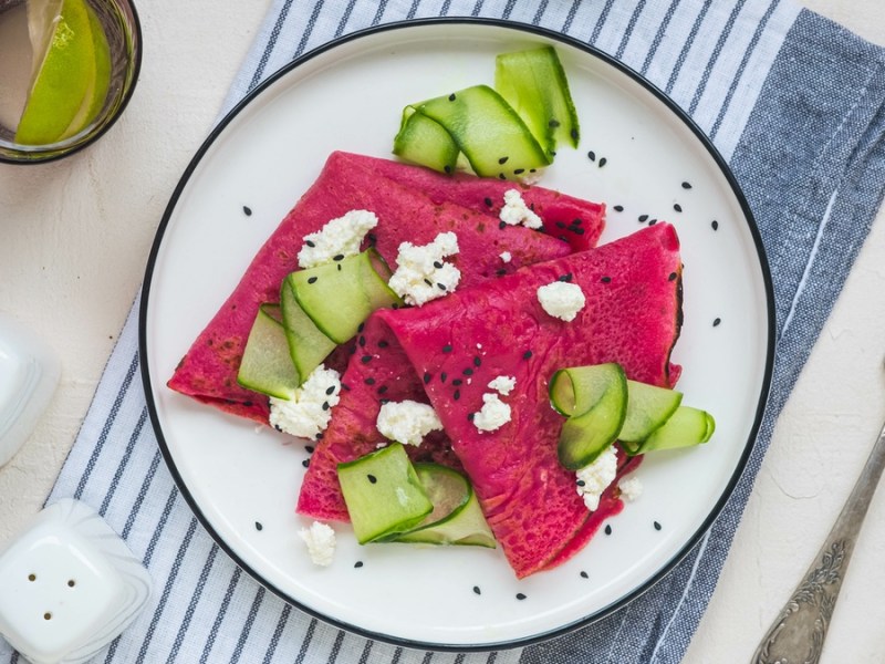 Rote-Bete-Pfannkuchen auf einem weißen Teller mit Gurken und Feta.