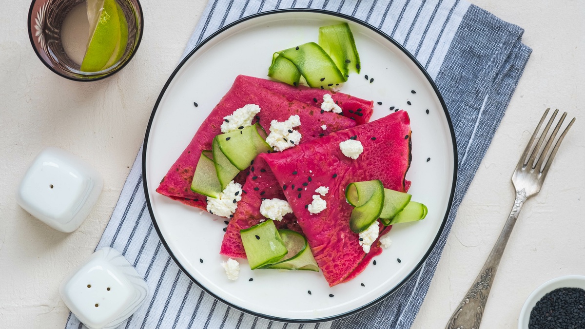 Rote-Bete-Pfannkuchen auf einem weißen Teller mit Gurken und Feta.