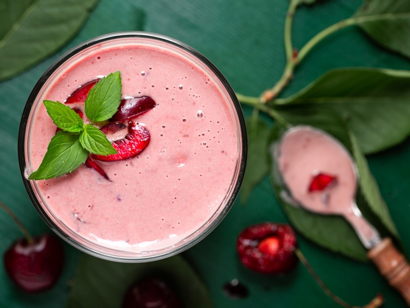 Sauerkirsch-Smoothie mit Minzblatt und Löffel daneben.