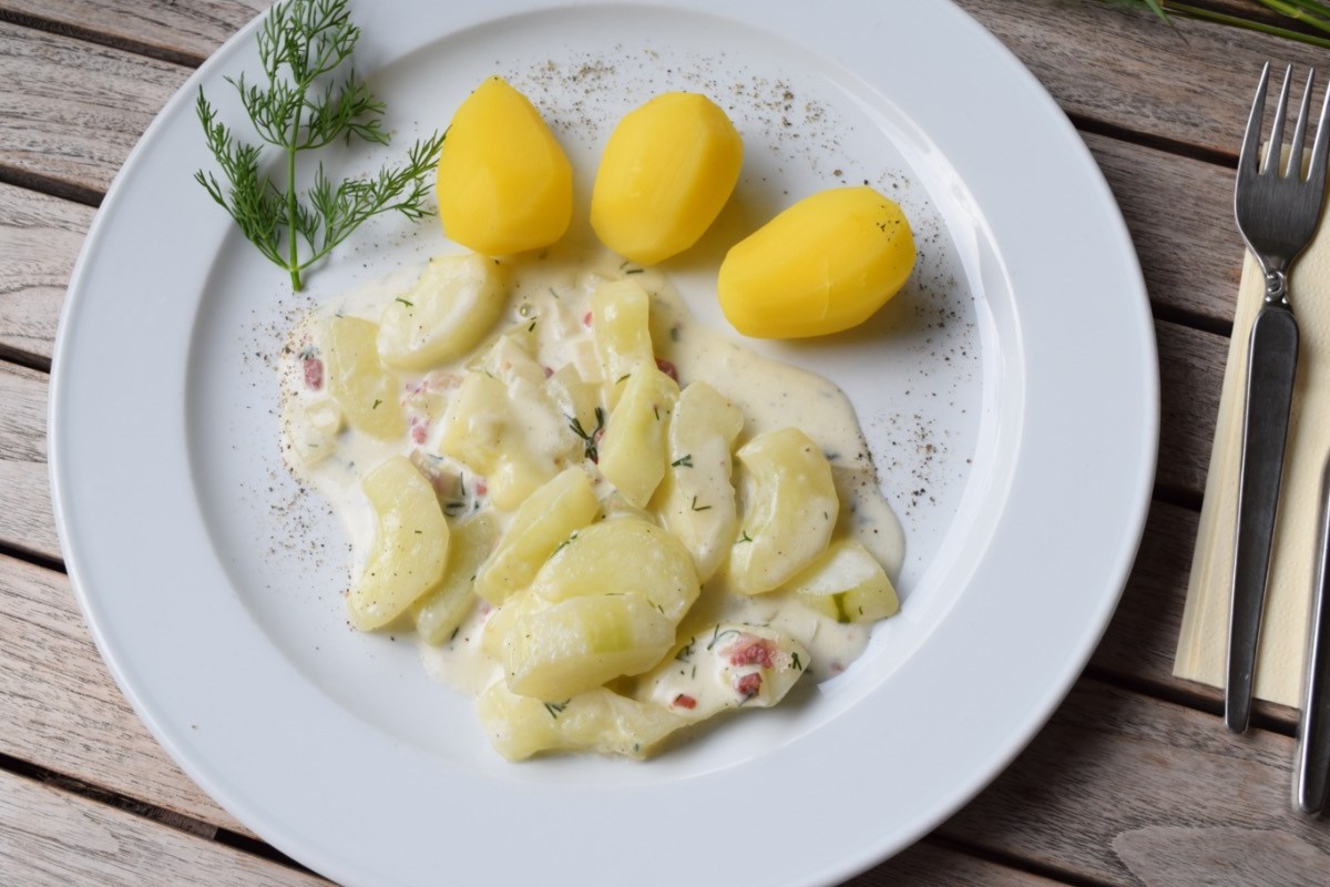 Rezept für Schmorgurken: Ein Teller mit Schmorgurken und Kartoffeln. Daneben liegt Besteck.