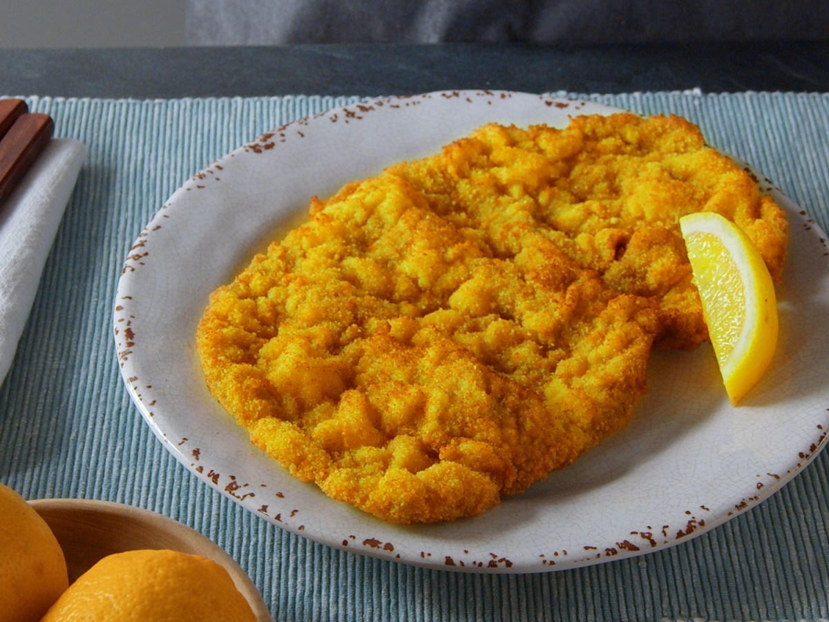 Schnitzel selbst machen: ein paniertes Schnitzel auf einem Teller, daneben Messer und Gabel.