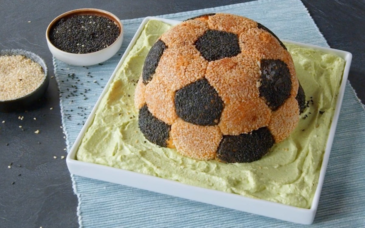 Ein Snack-Fußball auf einem rechteckigen Teller mit grünem Frischkäse.