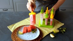 ein selbst gemachtes Wassermelonen-Eis wird von einer Frauenhand gehalten, daneben eine Schüssel mit Wassermelonenstückchen und mehr Eis.