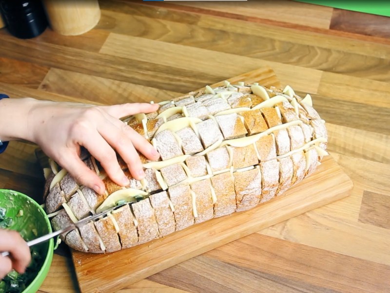 Ein Zupfbrot mit Käse und Knoblauchbutter auf einem Holzbrett.