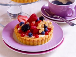 Ein Beeren-Tartelette mit Paradiescreme und verschiedenen Beeren auf einem Teller, daneben eine Tasse Kaffee auf Untertasse.