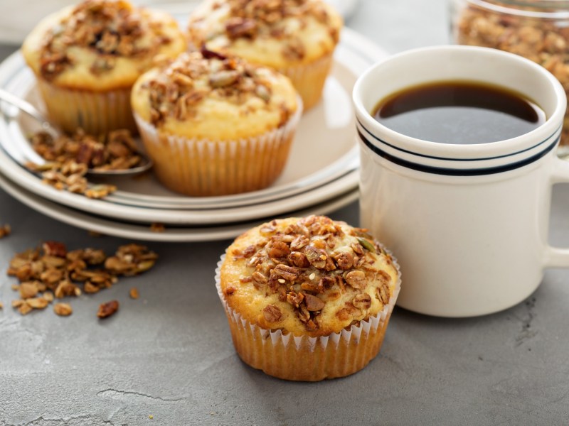 Cappuccino-Muffins auf einem Teller, einer steht davor, daneben eine Tasse Kaffee.