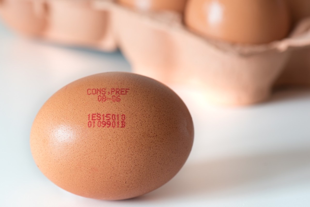 Ein braunes Ei mit Code im Vordergrund, dahinter Eier in einer Packung.