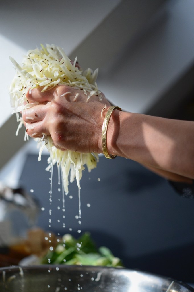 Erfolgreich Fermentieren: Zwei Hände drücken Flüssigkeit aus Sauerkraut.