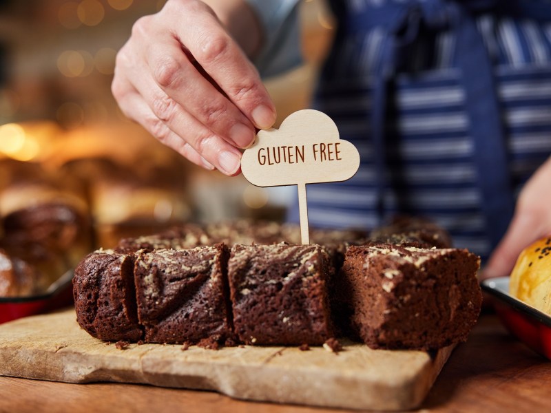 Glutenfreie Kuchen: Eine Hand steckt ein Label mit der Aufschrift "gluten free" in einen Schokokuchen.