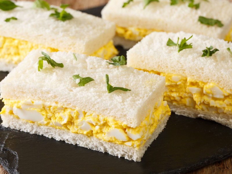 Mehrere japanische Ei-Sandwiches, Tamago Sando, auf einer Schieferplatte, garniert mit gehackter Petersilie.