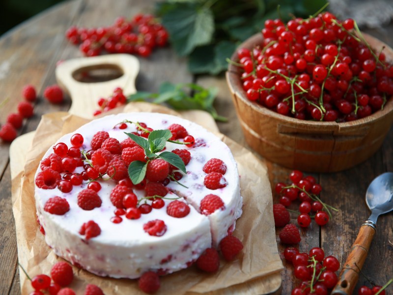 Eine Johannisbeer-Frischkäse-Torte auf einem Tisch voller Beeren.