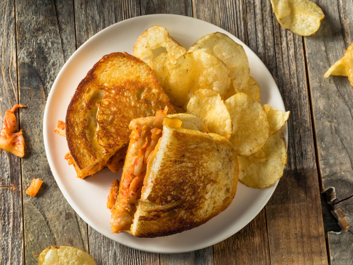 Grilled Cheese Sandwich mit Kimchi auf einem hellen Teller, serviert mit Kartoffelchips.