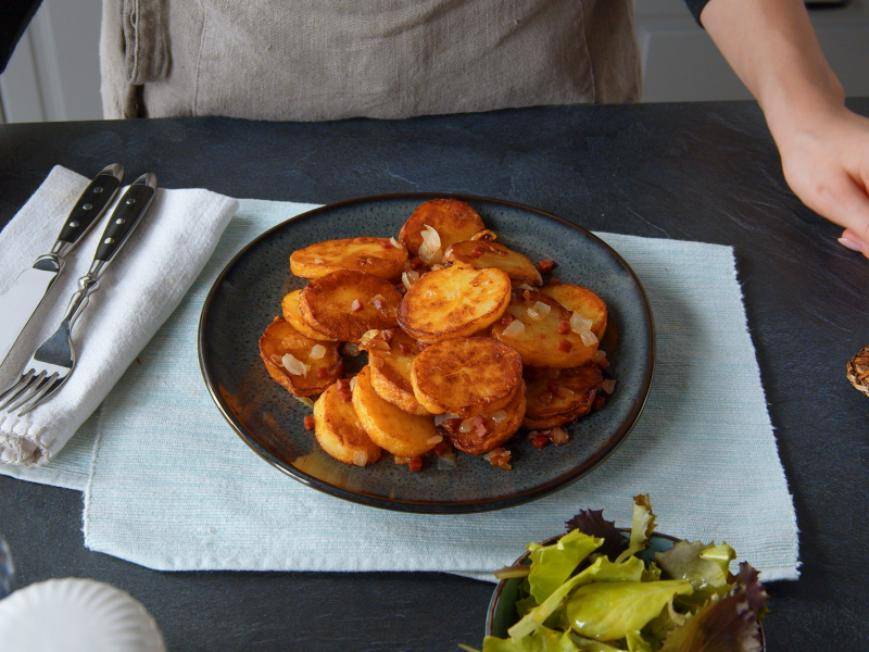 Knusprige Bratkartoffeln auf einem Teller, dahinter steht eine Köchin.