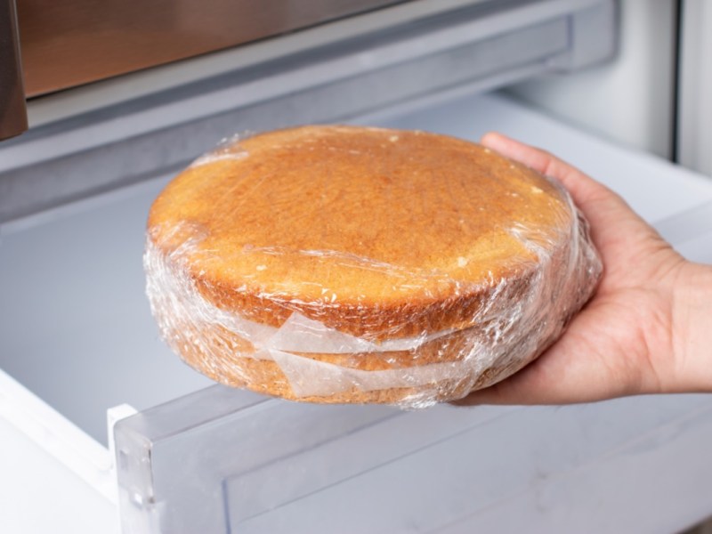Kuchen aufbewahren und einfrieren: Ein in Frischhaltefolie gewickelter Kuchen wird in den Gefrierschrank gelegt.