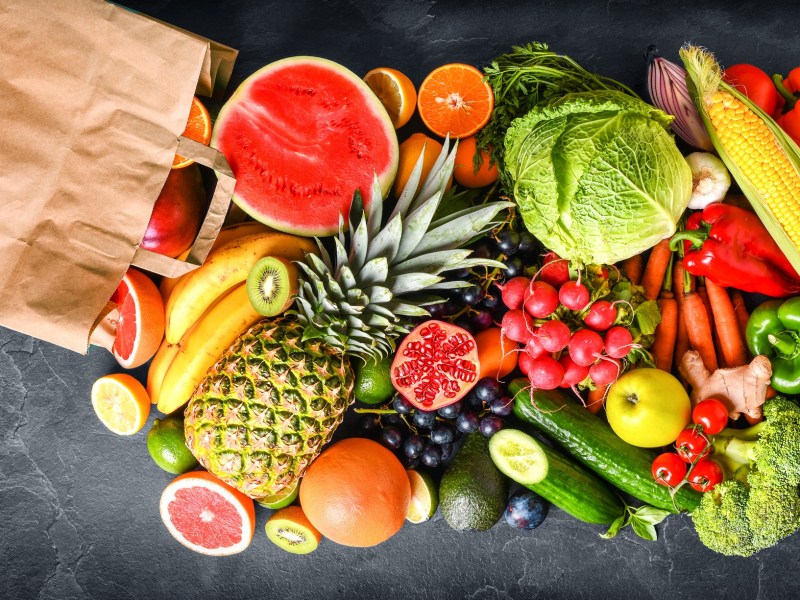 Kühlende Lebensmittel: Ein brauner Papierbeutel mit frischem Gemüse und Obst auf einem Tisch.