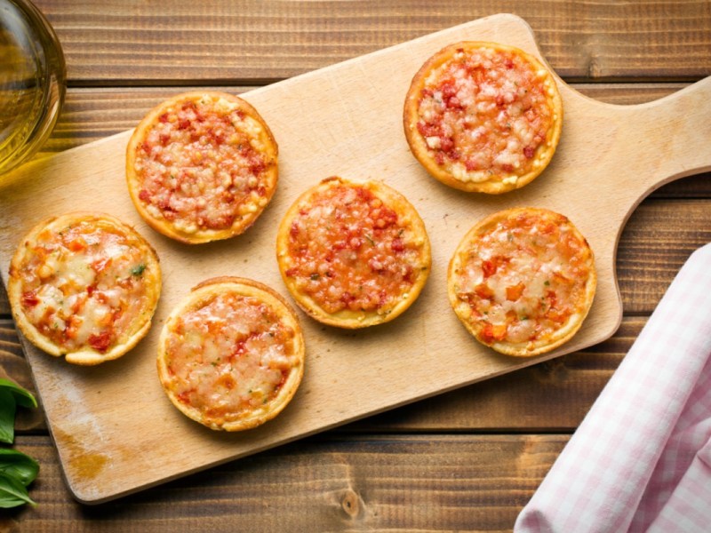 Sechs Mini-Pizzen auf einem Holzbrett in der Draufsicht.