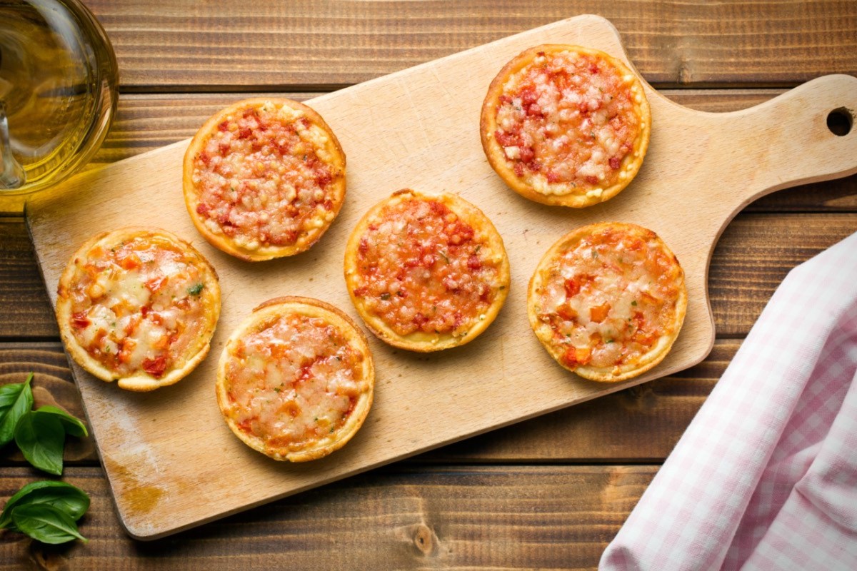 Sechs Mini-Pizzen auf einem Holzbrett in der Draufsicht.