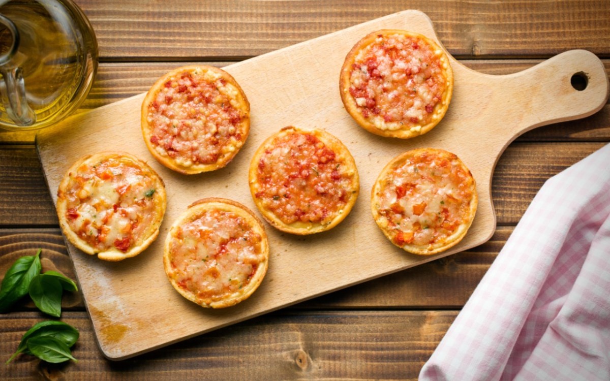 Sechs Mini-Pizzen auf einem Holzbrett in der Draufsicht.