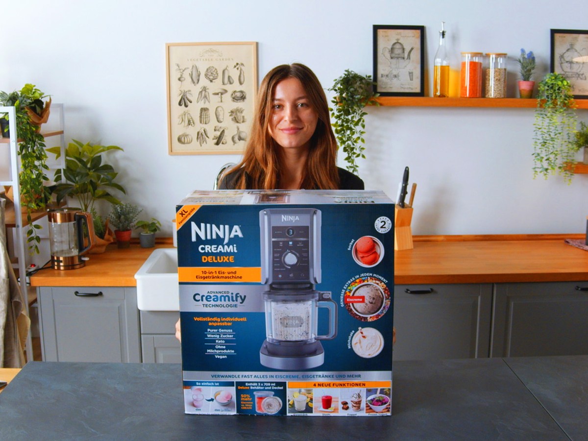 Ninja Creami Test: Die NInja Eismaschine verpackt in einer Küche, dahinter eine dunkelhaarige Frau.