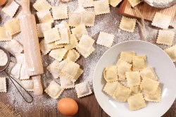 Ravioli selber machen: Selbstgemachte Ravioli auf einer Arbeitsfläche. Daneben liegen die Zutaten wie Ei und Mehl, sowie ein Nudelholz.