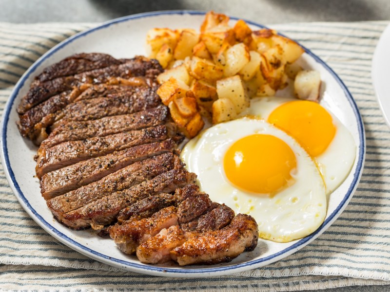 Steak and Eggs mit Kartoffel auf einem weißen Teller.
