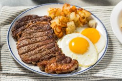 Steak and Eggs mit Kartoffel auf einem weißen Teller.