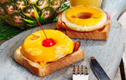 Zwei Stück Toast Hawaii auf einem grauen Marmorteller.