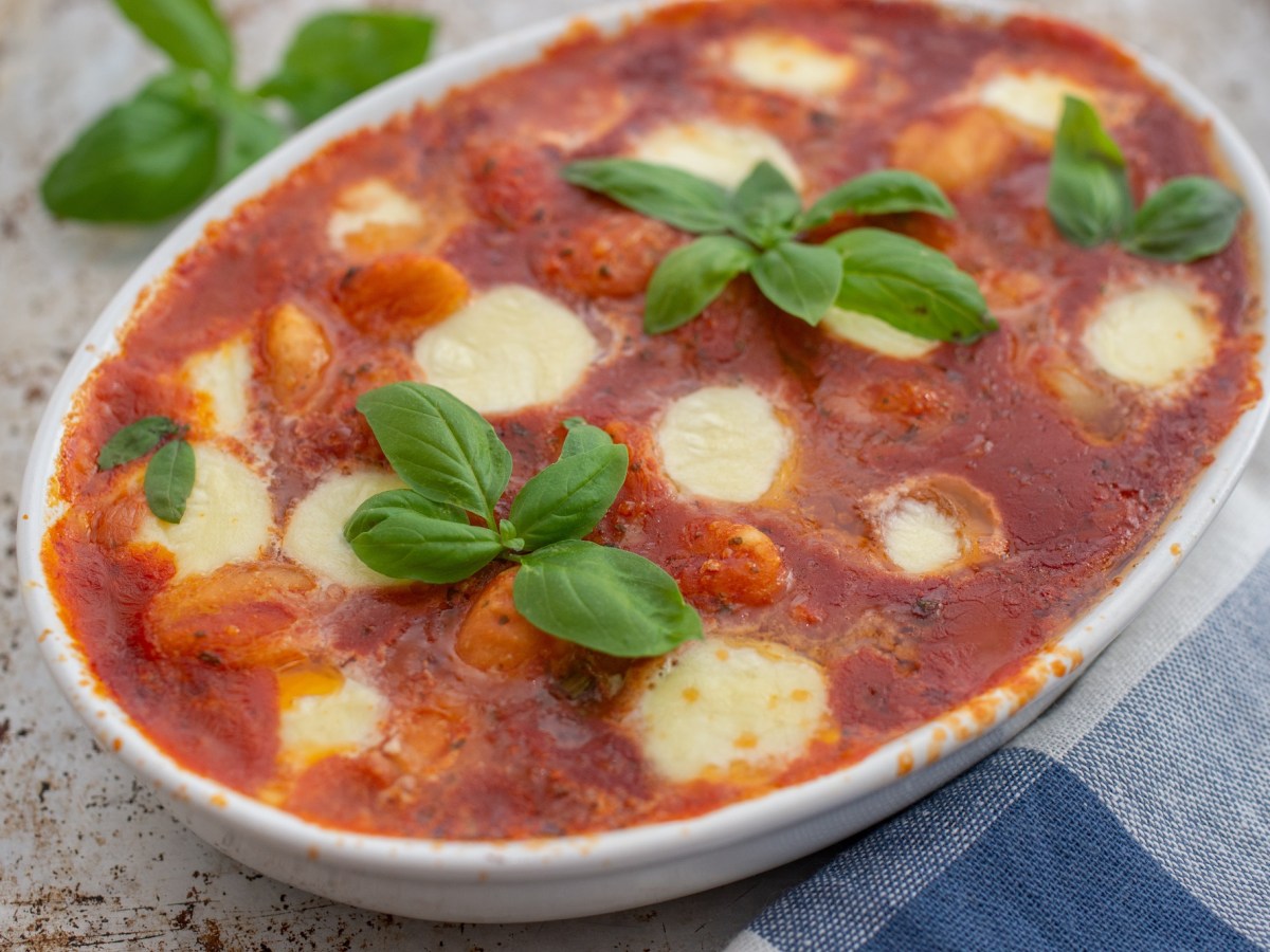 Gnocchi alla sorrentina: überbackene Gnocchi mit Tomatensoße und Mozzarella in einer Auflaufform, garniert mit Basilikum.