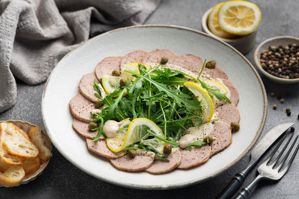 Vitello Tonnato auf einem weißen Teller, garniert mit Rucola und Zitrone.