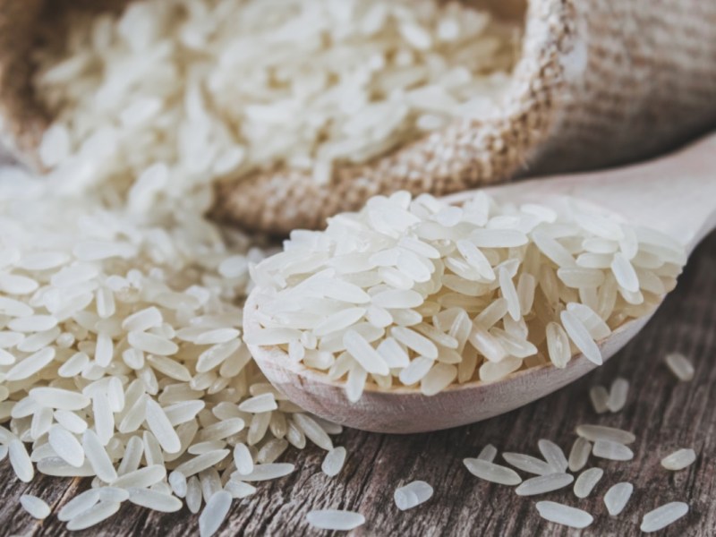 Wie viel Reis pro Person: ein Holzlöffel mit ungekochtem Reis, dahinter ein Sack mit Reis.