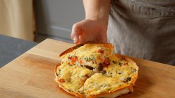 Wrap-Pizza mit Hüttenkäse, in vier Teile geschnitten, ein Stück wird in die Hand genommen.