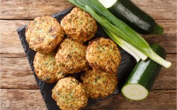 Mehrere Zucchini-Bällchen in der Draufsicht. Daneben liegen Zucchini und Frühlingszwiebeln.