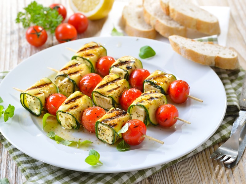 Zucchini-Grillspieße mit Feta auf einem weißen Teller.