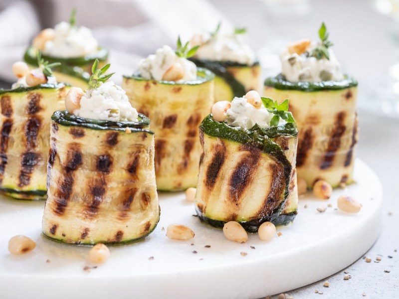 Zucchini-Röllchen mit Frischkäse auf einem Tablett.