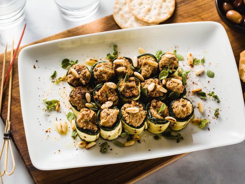 Zucchini-Röllchen mit Olivencreme auf einem Tablett.