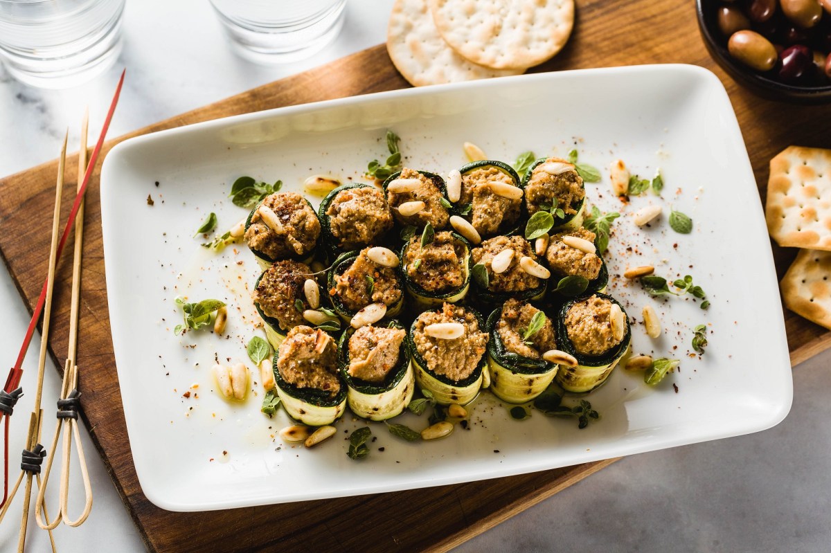 Zucchini-Röllchen mit Olivencreme auf einem Tablett.