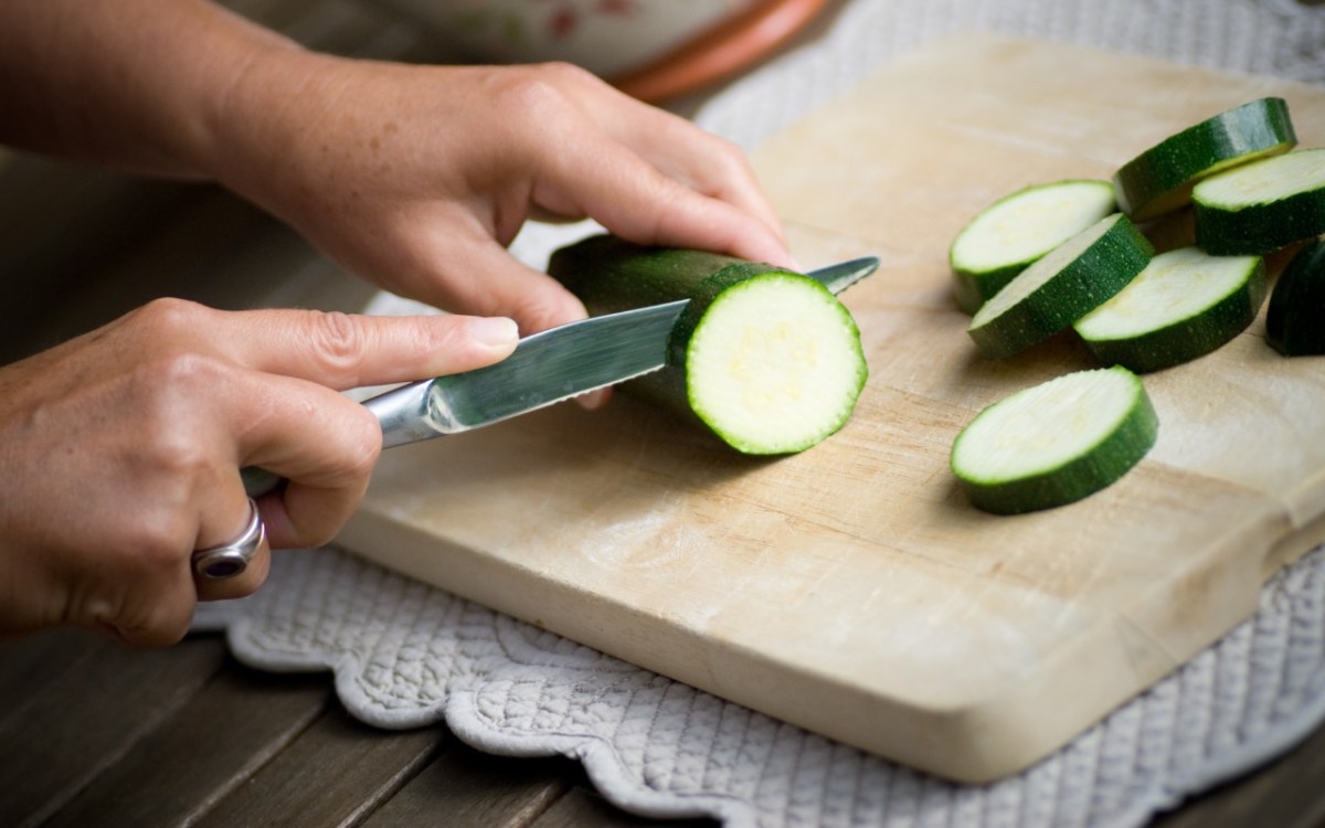 Zucchini zubereiten: Eine Zucchini wird auf einem Holzbrett in Scheiben geschitten.