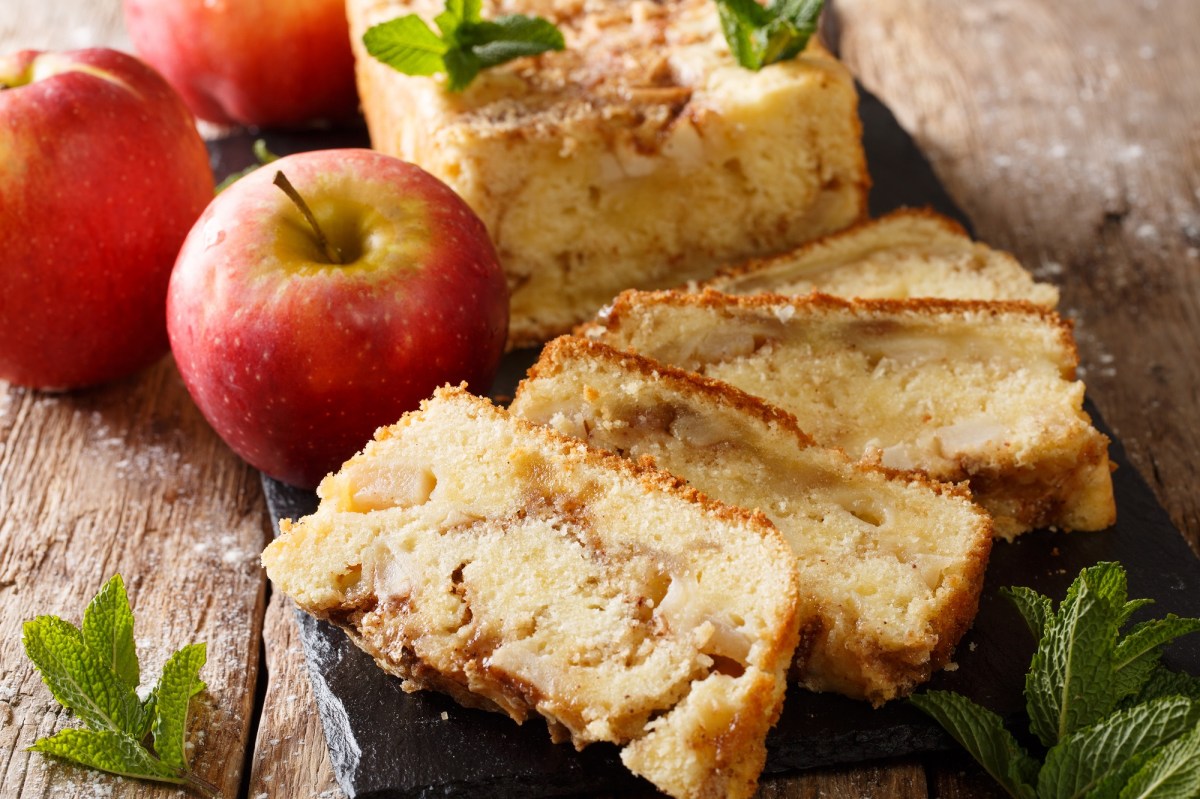 angeschnittener Apfelkuchen aus der Kastenform, daneben ganze Äpfel.