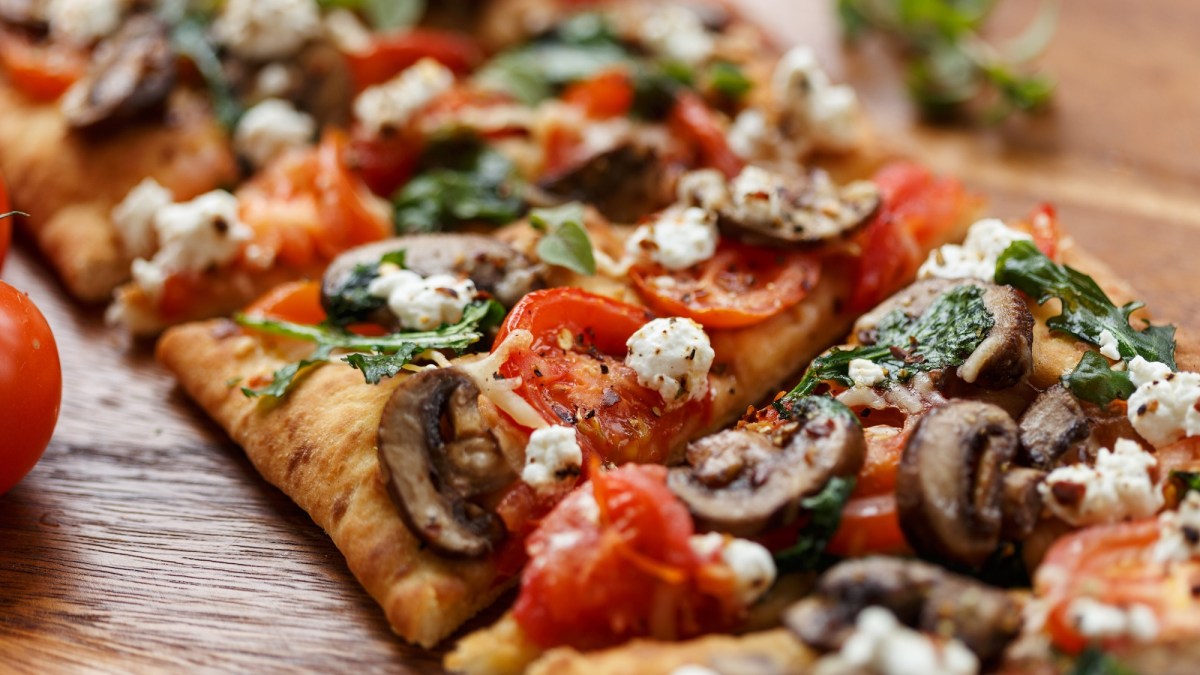 In StÃ¼cke geschnittene Fladenbrot-Pizza mit Pilzen, Feta und Tomaten.