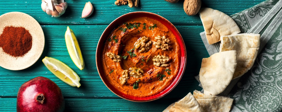 Schale Granatapfel-Paprika-Dip mit Fladenbrot Zitrone und Gewürze daneben.