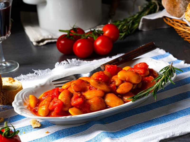 dicke Bohnen in Tomatensoße auf einem ovalen Teller.