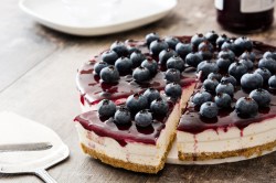 Ein Heidelbeer-Quarkkuchen, von dem ein Stück abgeschnitten wird, auf einem weißen Teller.