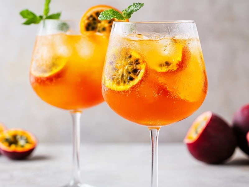 Zwei Gläser Maracuja Spritz mit Orangen- und Maracujascheiben.