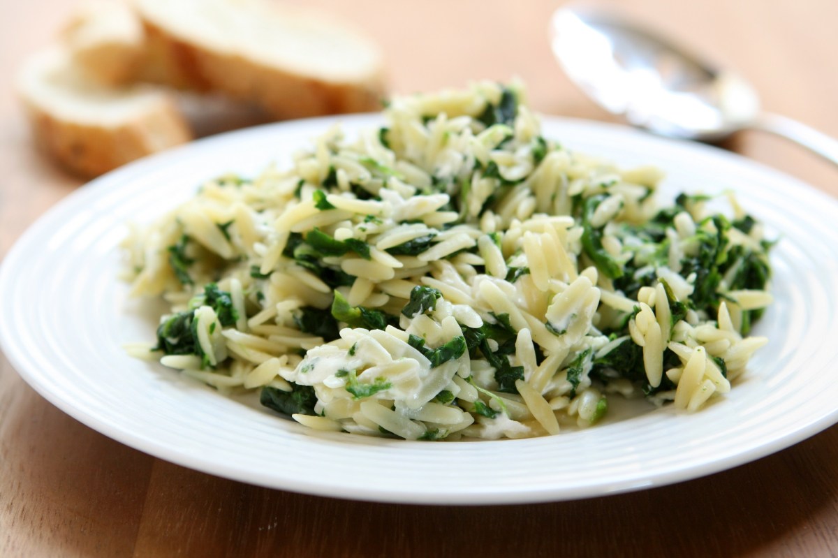 Ein Teller Orzo-Nudeln mit Spinat und Feta, daneben ein Löffel und Baguettescheiben.