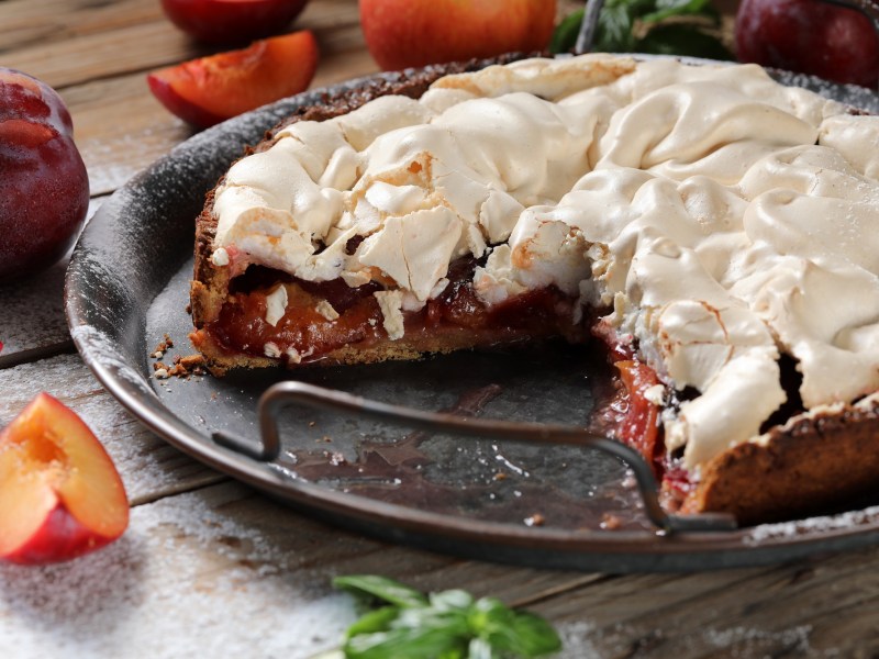 angeschnittener Pflaumenkuchen mit Baiser auf Kuchenplatte